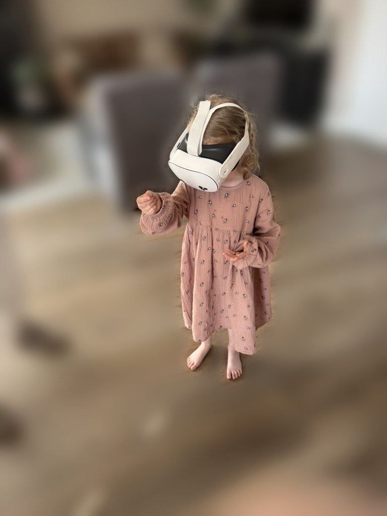Klein meisje in roze jurkje met VR-bril op, op blote voeten in de woonkamer